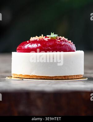 Delicate dessert rests on rustic wooden surface. Creamy white base contrasts with vibrant red topping. Golden crust adds texture beneath the cake. Tin Stock Photo