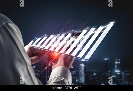A business professional examines financial data on a smartphone, showcasing digital graphs that signify growth against an urban night backdrop. Impute Stock Photo