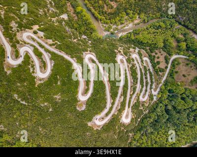 Aerial view of a zigzag road winding through a dense green forest with ...