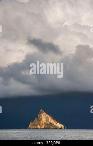 Storm clouds form over the volcanic sea stack of Strombolicchio near the island of Stromboli, Italy. The island, was the volcanic plug thrown out of the Stromboli volcano during a massive explosion 200,000 years ago. Stock Photo