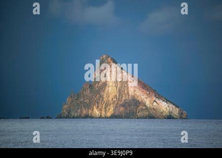 Storm clouds form over the volcanic sea stack of Strombolicchio near the island of Stromboli, Italy. The island, was the volcanic plug thrown out of the Stromboli volcano during a massive explosion 200,000 years ago. Stock Photo