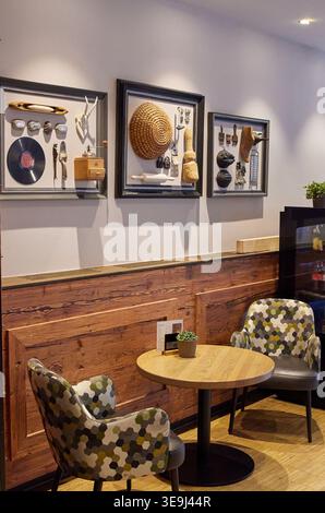 Cozy cafe interior with wooden walls, stylish armchairs, and 3D framed wall art featuring vintage objects and a straw hat. Stock Photo
