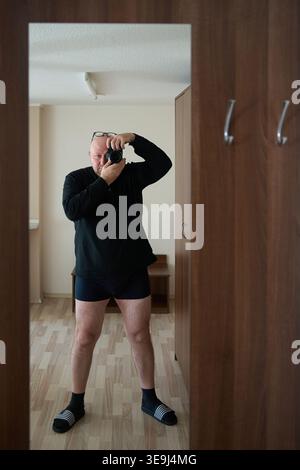 Man in black sweater taking a mirror selfie with a camera in a hallway. Reflection in a large mirror on a wooden wardrobe Stock Photo
