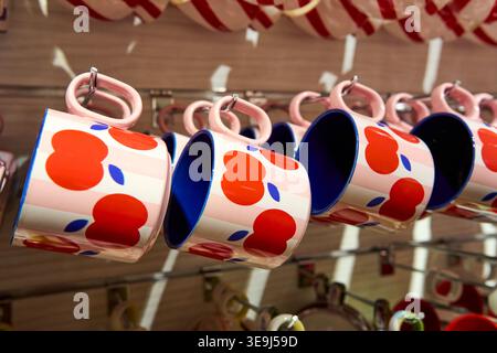 Ceramic mugs with a vibrant red apple pattern and deep blue interior hanging on display. Stylish and modern kitchenware design. Stock Photo