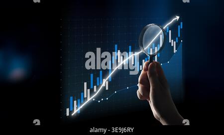 A hand holds a magnifying glass over a financial chart displaying a rising trendline, emphasizing the importance of analysis and insight in business Stock Photo