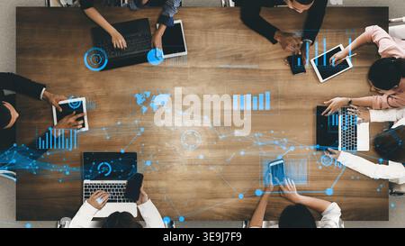 A diverse business team collaborates using digital devices on a wooden table. Dynamic data visualization and technology enhance their brainstorming Stock Photo