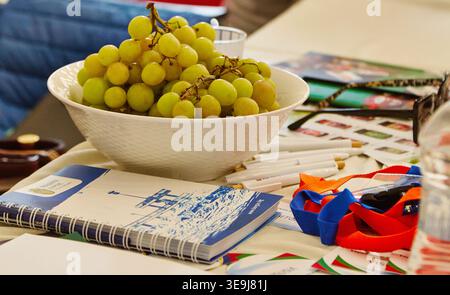 Burgas, Bulgaria - April 17, 2026: Bowl filled with green grapes placed on a table with various promotional items and colorful ribbons at an exhibitio Stock Photo