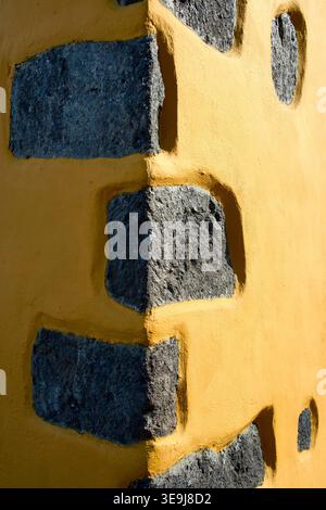 Close-up of a corner wall with grey stones embedded in yellow plaster. Traditional Mediterranean architectural detail with rough texture. Stock Photo