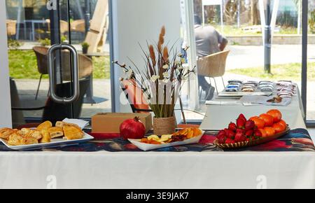 Assorted food items such as pastries and fruits arranged on a table at a public exhibition, with outdoor seating and greenery in the background Stock Photo