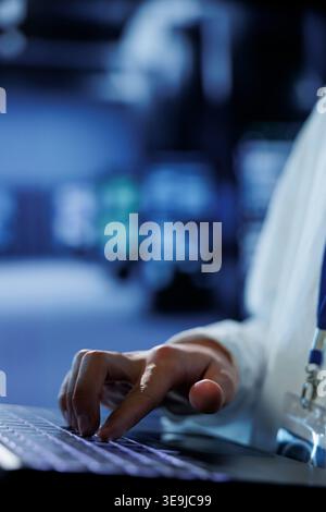 Knowledgeable admin in data center uses laptop to prevent system overload during peak traffic periods. Adept expert in server hub ensuring enough network bandwidth for smooth operations, close up Stock Photo