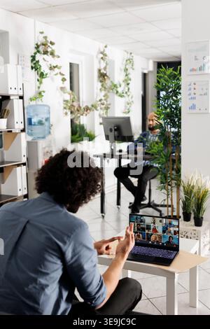 Project manager communicating with coworkers via video call to discuss work progress. Employees team talking about company growth strategy in online meeting using laptop in office Stock Photo