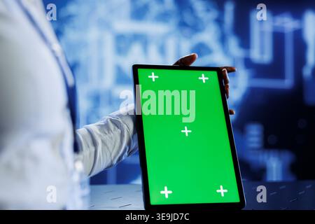 IT consultant uses green screen tablet to update neural networks, writing intricate binary code scripts on tablet. Worker uses chrome key device programming to upgrade AI simulation model Stock Photo
