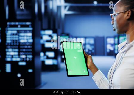 Technician in server room using green screen tablet to future proof network from downtimes and unexpected system failures. Expert with chrome key device ensuring increased data security Stock Photo