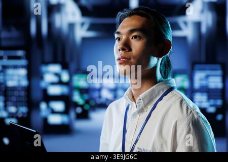 Certified technician in data center uses laptop to prevent system overload during peak traffic periods. Proficient employee in server room ensuring enough network bandwidth for smooth operations Stock Photo