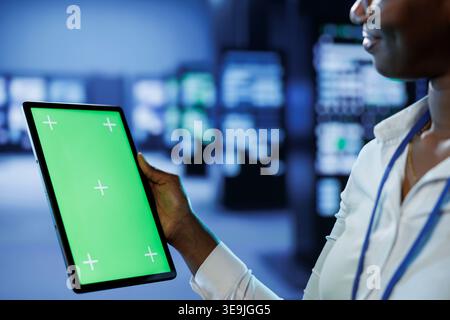 Trained technician in server room using mockup tablet to future proof network from downtimes and unexpected system failures. Expert with isolated screen device ensuring increased data security Stock Photo