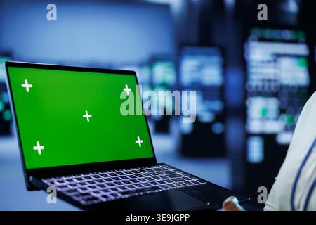 Admin in data center uses mockup laptop to prevent server machines overload. Expert between server mainframes using isolated screen device to ensure enough network bandwidth for smooth operations Stock Photo