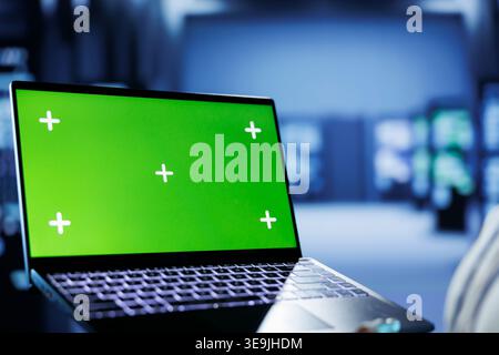 Admin in cloud computing business uses mockup laptop to prevent server machines overload. Expert between rackmounts using green screen device to enable enough network bandwidth for smooth operations Stock Photo