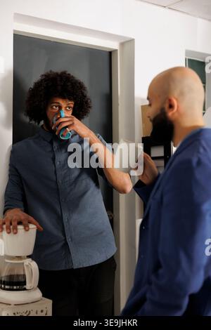 Arab colleagues enjoying friendly conversation over coffee during break in corporate office. Two young company employees discussing project strategy ideas in coworking space Stock Photo