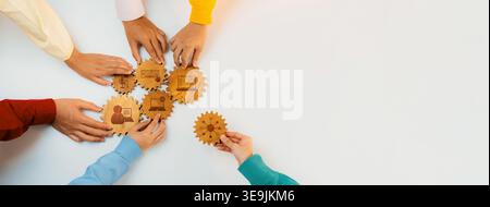Diverse hands interacting with wooden gears, symbolizing teamwork and collaboration in a vibrant office setting, showcasing the spirit of collective Stock Photo