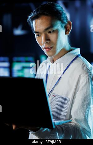 Dara center knowledgeable professional running code and programming on laptop, troubleshooting and upgrading high tech facility designed to accommodate rows of fully operational server electronics Stock Photo