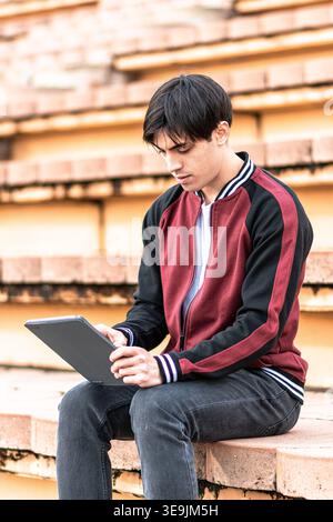 Young student concentrating on tablet sitting on campus stairs Stock Photo