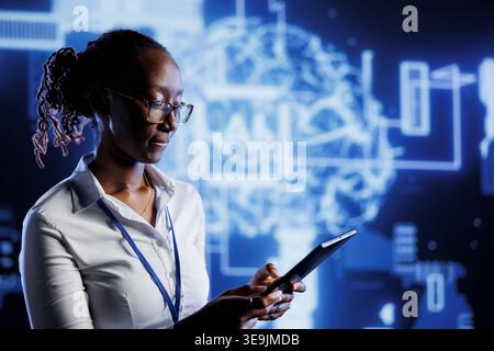 African american admin writes code on tablet to visualize artificial intelligence neural networks using augmented reality. High tech workspace supervisor runs AI script for information processing Stock Photo