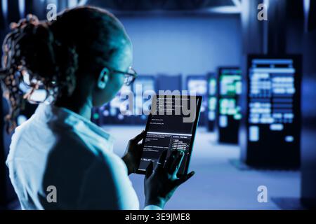Computer scientist builds firewall protection systems in server room housing advanced infrastructure. High tech facility manager runs code on tablet to upgrade data center rigs Stock Photo