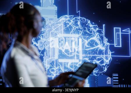 System administrator updates neural networks made of interconnected nodes, writing intricate binary code scripts on tablet. High tech facility worker uses programming to upgrade AI simulation model Stock Photo