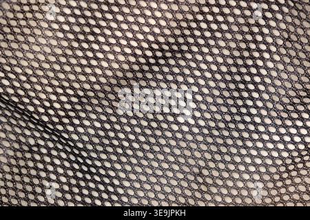 Close-up of black mesh fabric with uniform oval perforations and soft folds creating a textured pattern Stock Photo