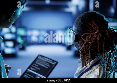 Team of engineers building firewall systems in server room housing advanced infrastructure. Capable employees running code on tablet to upgrade data center rigs handling demanding workloads Stock Photo