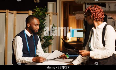 African american tailors team in atelier, working together to create modern fashion collection. Business owner and assistant designing clothes using textile industry tools in workshop. Stock Photo