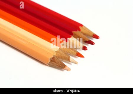 Close-up of a row of sharpened coloured pencils in warm red tones on a white background Stock Photo