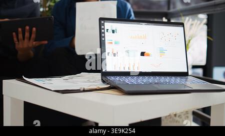 Two coworkers planning new strategy and analyzing online company information in startup office. Business partners collaborating on analytics presentation, using laptop and papers. Stock Photo