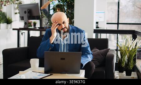 Analyst working with headache in office, feeling unwell and overworked at executive job. Sick businessman not being able to think properly because of painful migraine, project burnout. Stock Photo