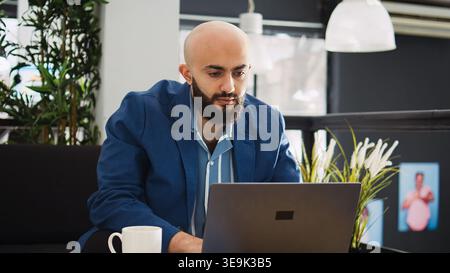 Manager comparing data on laptop and working in startup coworking space. Small business employee standing near workstation, analyzing statistics report for programming. Agency CEO. Stock Photo