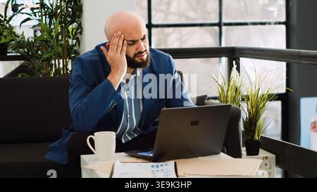 Analyst dealing with headache at work, trying on examine annual data strategy but feeling unwell. Sick employee working on development project with migraine, being overworked. Handheld shot. Stock Photo