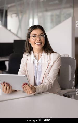 Woman in elegant suit sitting at desk using digital tablet Stock Photo