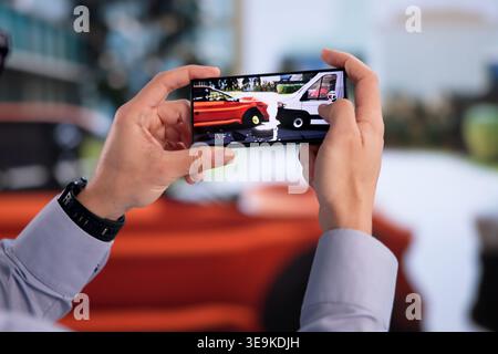 Hispanic Insurance Agent Examines Vehicle Damage With Smartphone Post-Crash Stock Photo