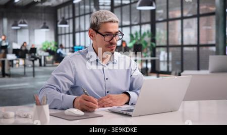 Engaged Hispanic Businessman Attending Virtual Webinar On Laptop With Headphones Stock Photo