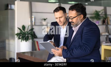 Two focused professionals using tablet working together on digital tasks Stock Photo