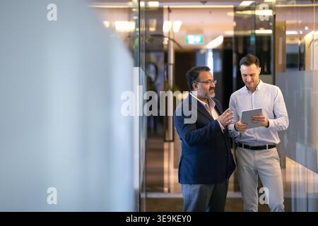 Two office employees discussing information on tablet in hallway Stock Photo