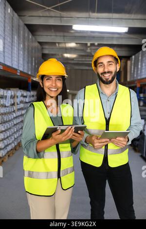 Workers in helmets and vests standing in industrial warehouse aisle Stock Photo