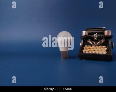 Miniature black vintage typewriter and a white lightbulb on a blue background. Stock Photo