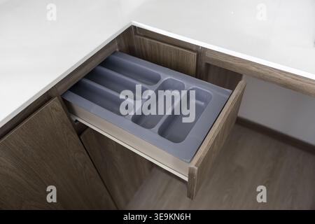 Open wooden kitchen cabinet drawer revealing an empty grey plastic organizer tray for cutlery storage conveying calm peaceful clean domestic lifestyle Stock Photo