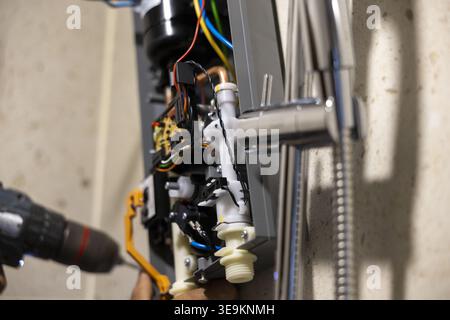 Plumber working with focused determination to install electric water heater in modern bathroom using power drill on wall fixing wire and shower hose p Stock Photo