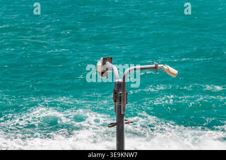 Security surveillance cameras on metal pole above turquoise sea with waves Stock Photo