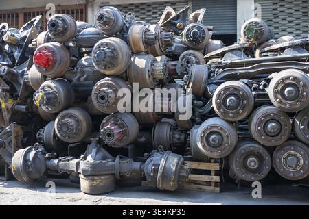 Large pile of used heavy truck axles differentials and suspension components stacked outdoors in junkyard or salvage yard representing industrial recy Stock Photo