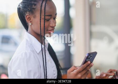 Close portrait of young Black woman using smartphone at an outdoor cafe, focused on the screen. Mobile messaging, online browsing, digital communicati Stock Photo