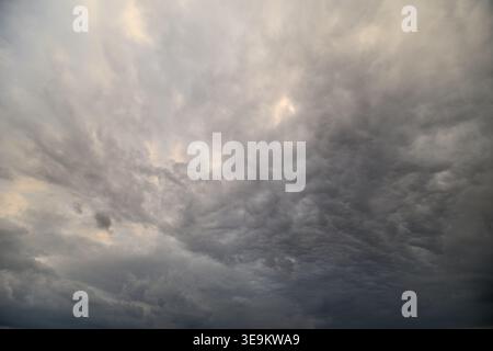 Dramatic storm clouds filling sky, layered textured formations with rolling mammatus pockets, muted gray palette, low diffused light, heavy looming at Stock Photo