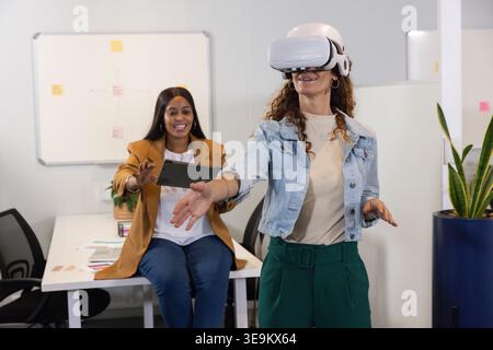 Diverse female coworkers testing VR headset and interacting at office desk with tablet, copy space Stock Photo